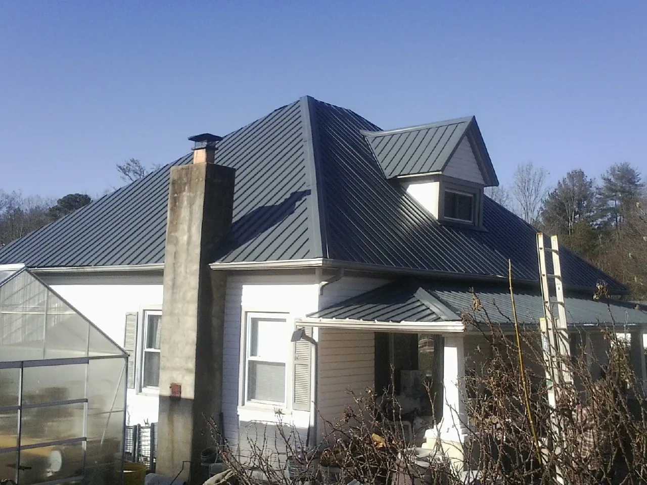 Dark blue standing seam metal roof on a white farmhouse with dormer — Slate & Tile Roof Repair by Roofing Brothers in Center Valley