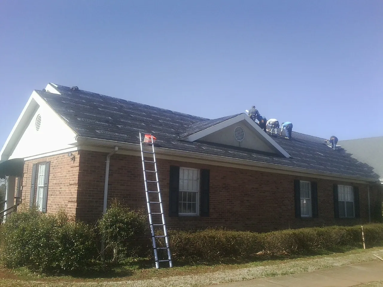 Crew tearing shingles off a brick ranch roof with a ladder set — Emergency Roof Repair work by our crew in Center Valley