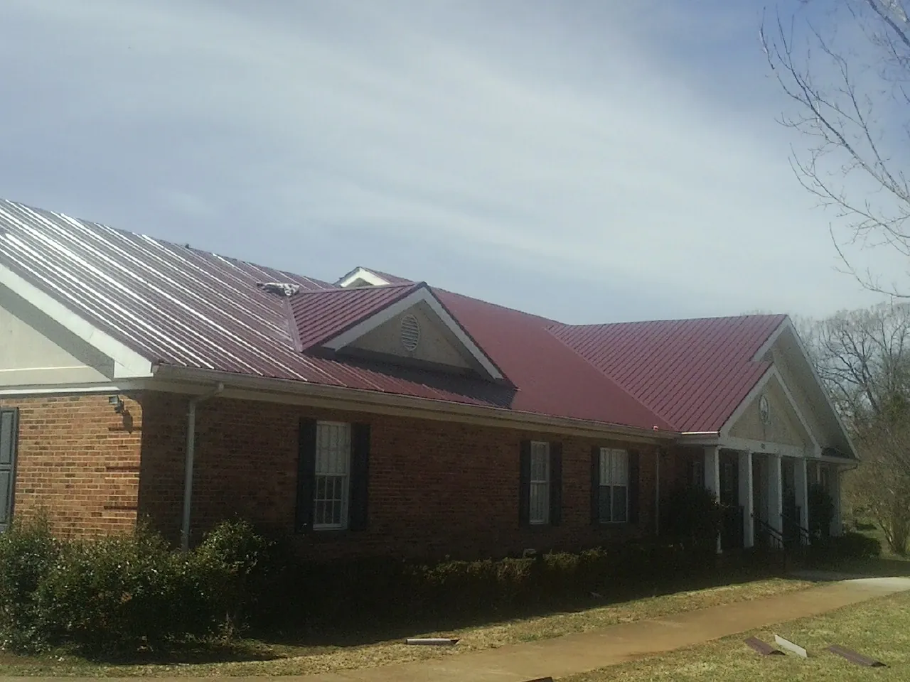 Red metal roof with gabled entries on a long brick building, from a Hail Damage Roof Repair job in Center Valley