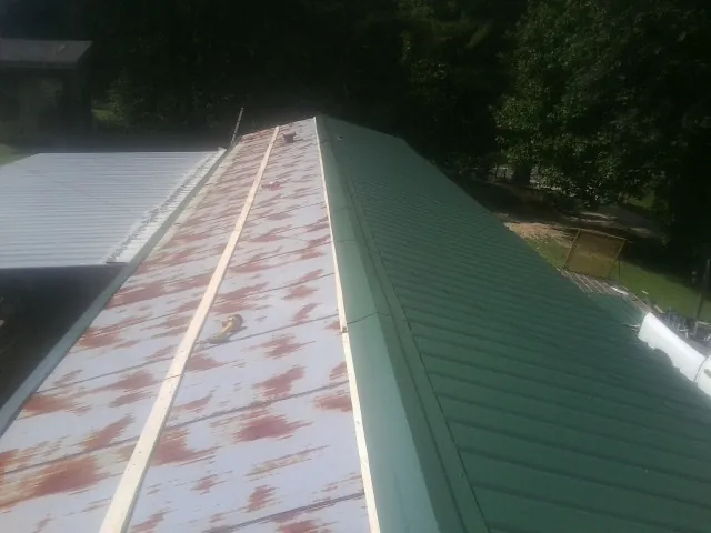 Old rusted panels beside newly installed green metal roofing — Wind Damage Roof Repair by Roofing Brothers in Center Valley