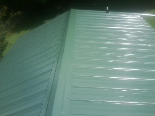 New green metal panels meeting at the ridge of a roof — Flat Roof Repair work by our crew in Center Valley