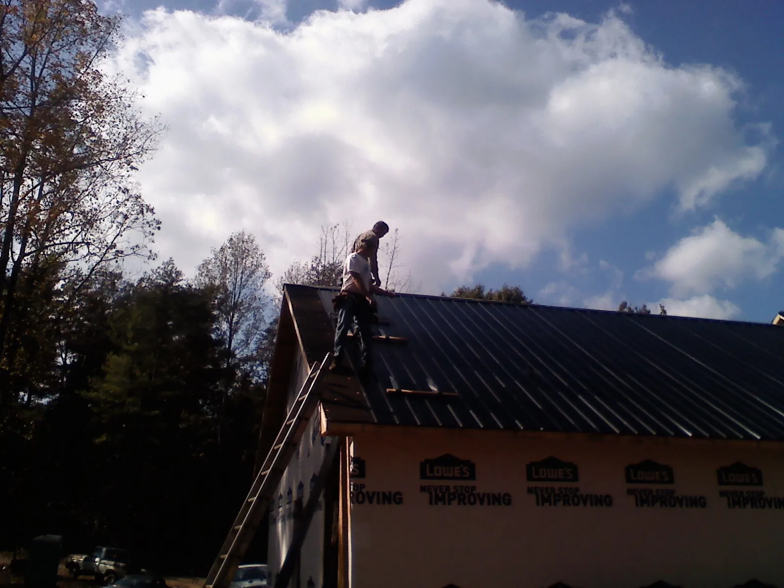 Roofer fastening dark metal panels high against a cloudy sky, from a Roof Inspection job in Center Valley