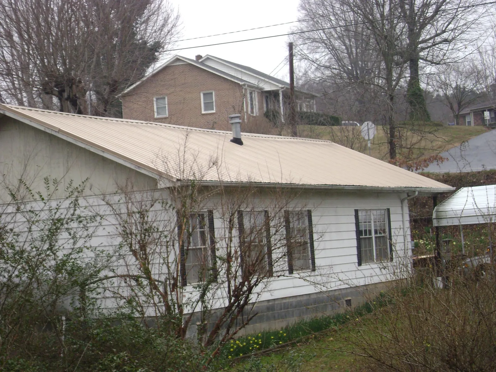 Tan metal roof on a white sided house set into a hillside — Commercial Roofing by Roofing Brothers in Center Valley